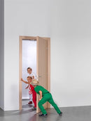 an image showing three children in white, red and green clothing interacting with a beige wooden door