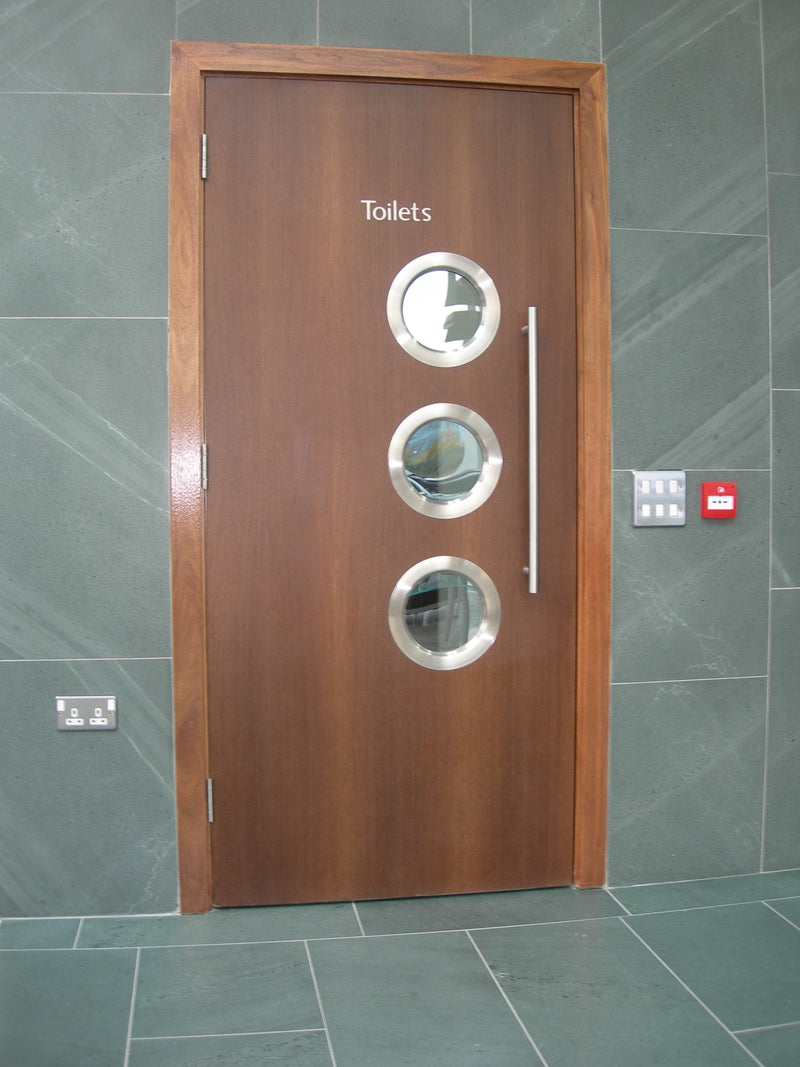 an image of a brown wooden door with three round silver slimport vision panels on a green tiled background